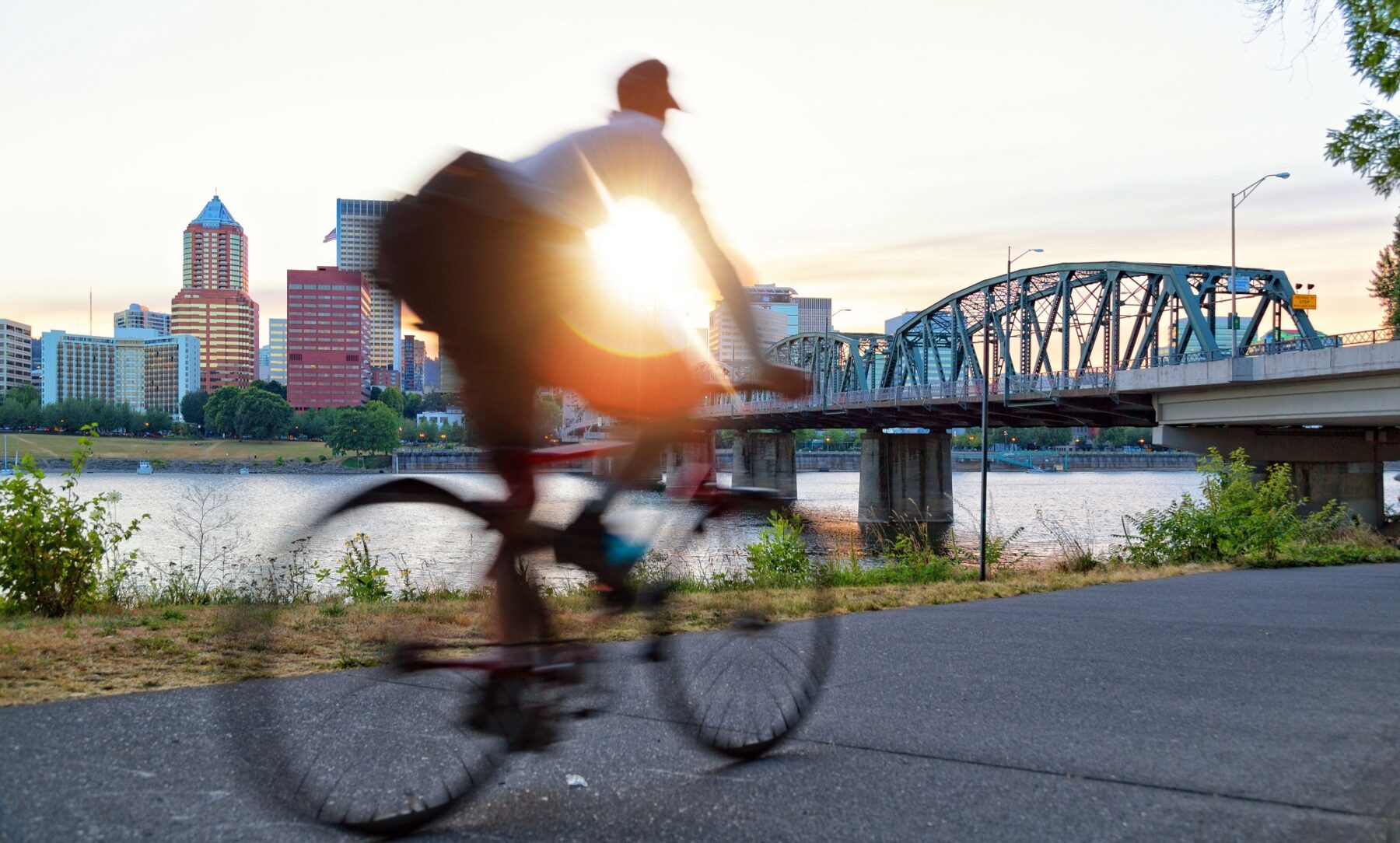 person riding a bike and in the background is a sunset and a bridge