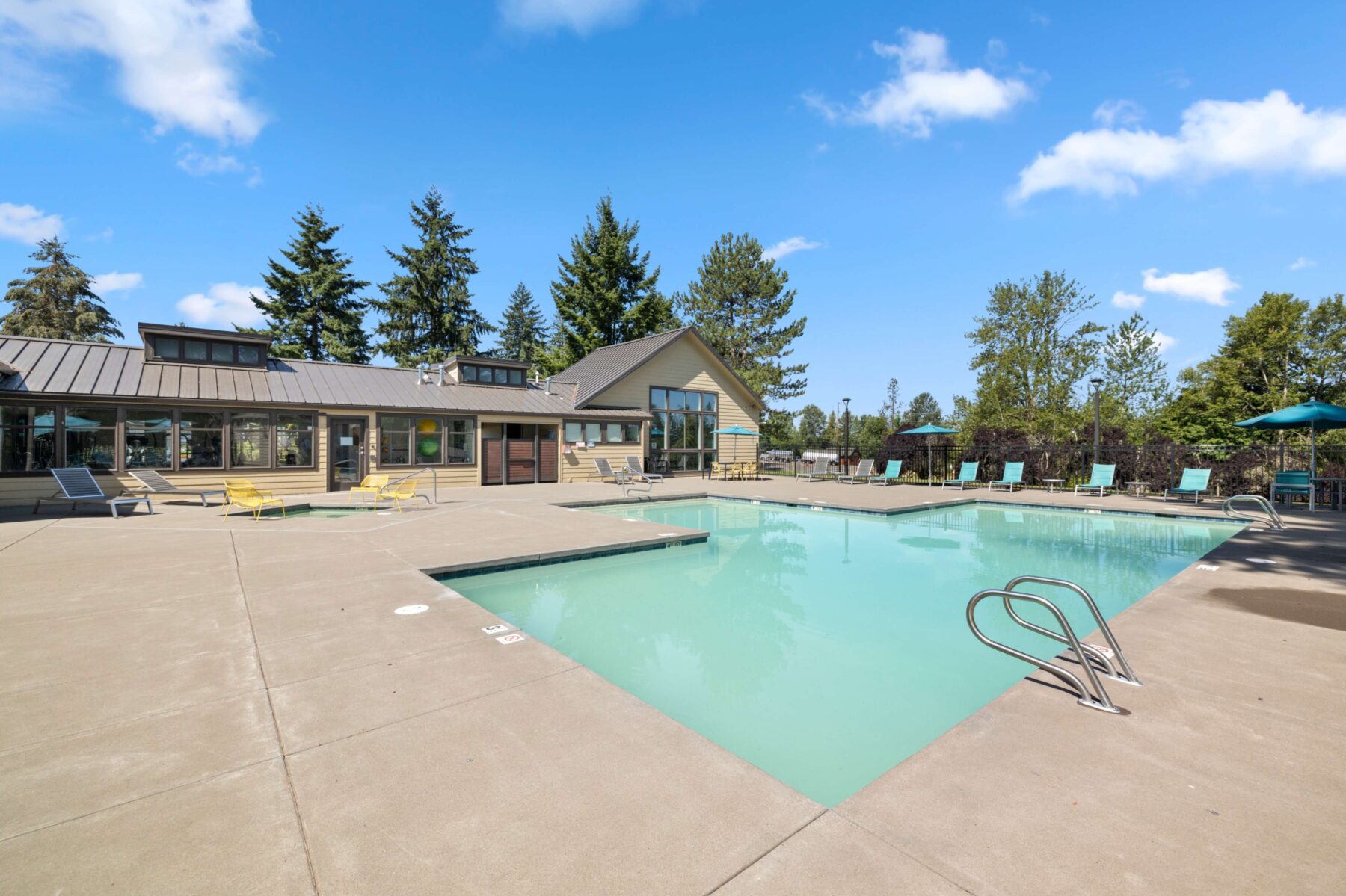 Pool with deck chairs, tables with umbrellas, and large trees